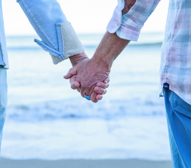 Two people holding hands in front of a calm ocean, symbolizing love, connection, and acceptance.